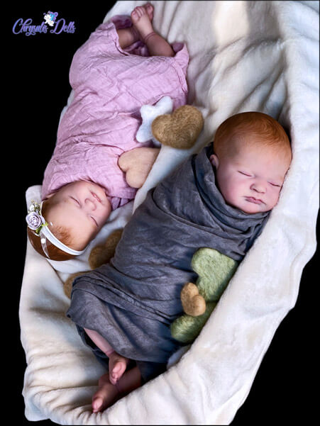 Reborn Max twins sleeping in a basket together; Both the boy and girl have ginger hair and a fare, rose complexion.