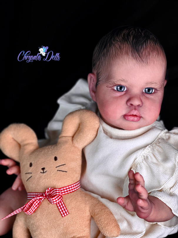 Reborn Ellie leans back, holding a yellow bunny with red bow. She is looking off to the side with her big blue eyes.